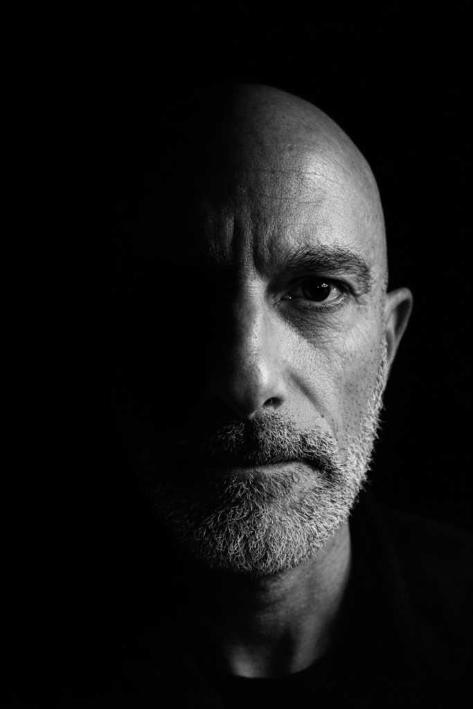 Ritratto in bianco e nero split lighting, contrasto drammatico, riflessione su identità e umanità.